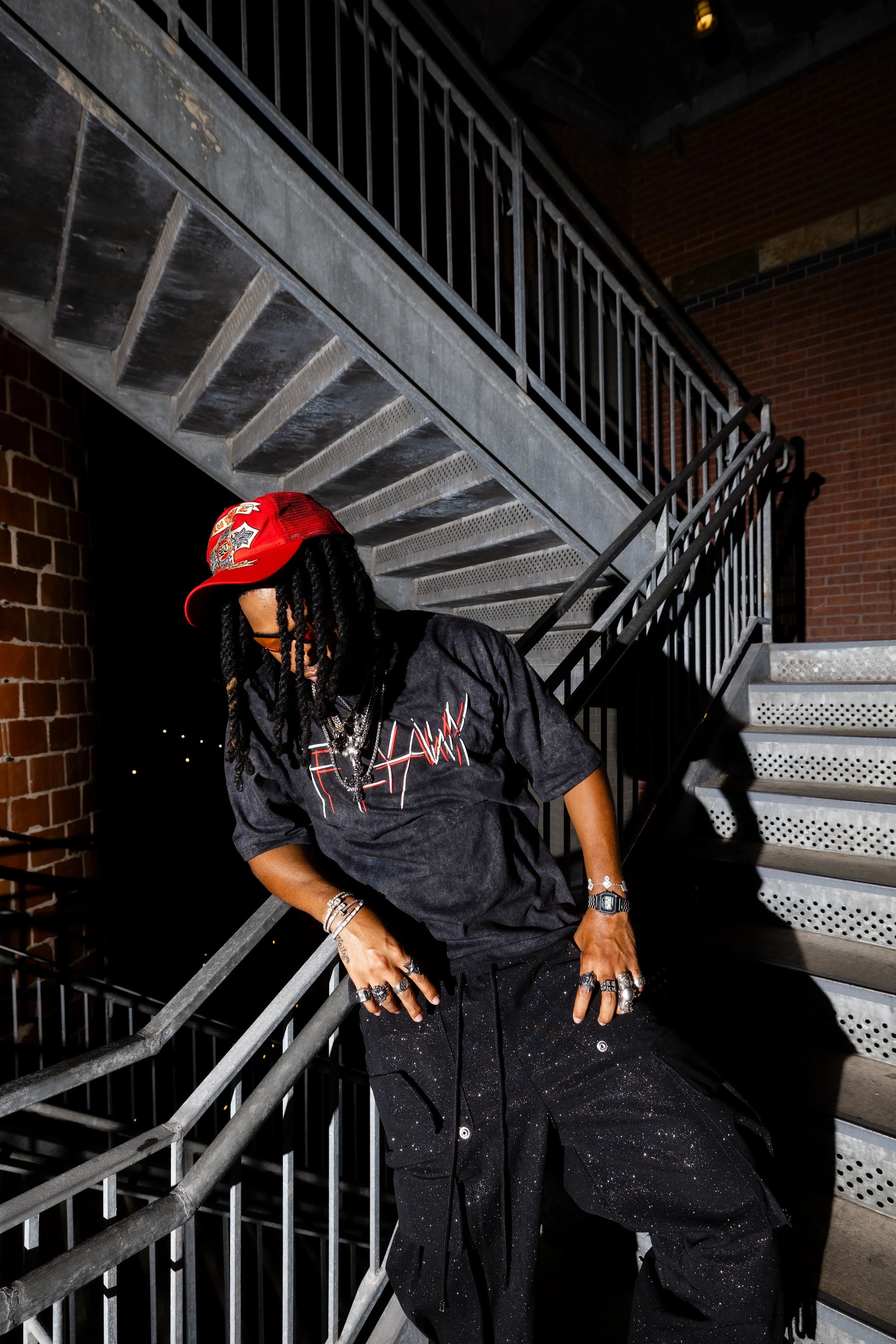 Oversized black acid-washed tee with red "Bloodstatic" graphic in jagged font, styled with black pants and red cap.