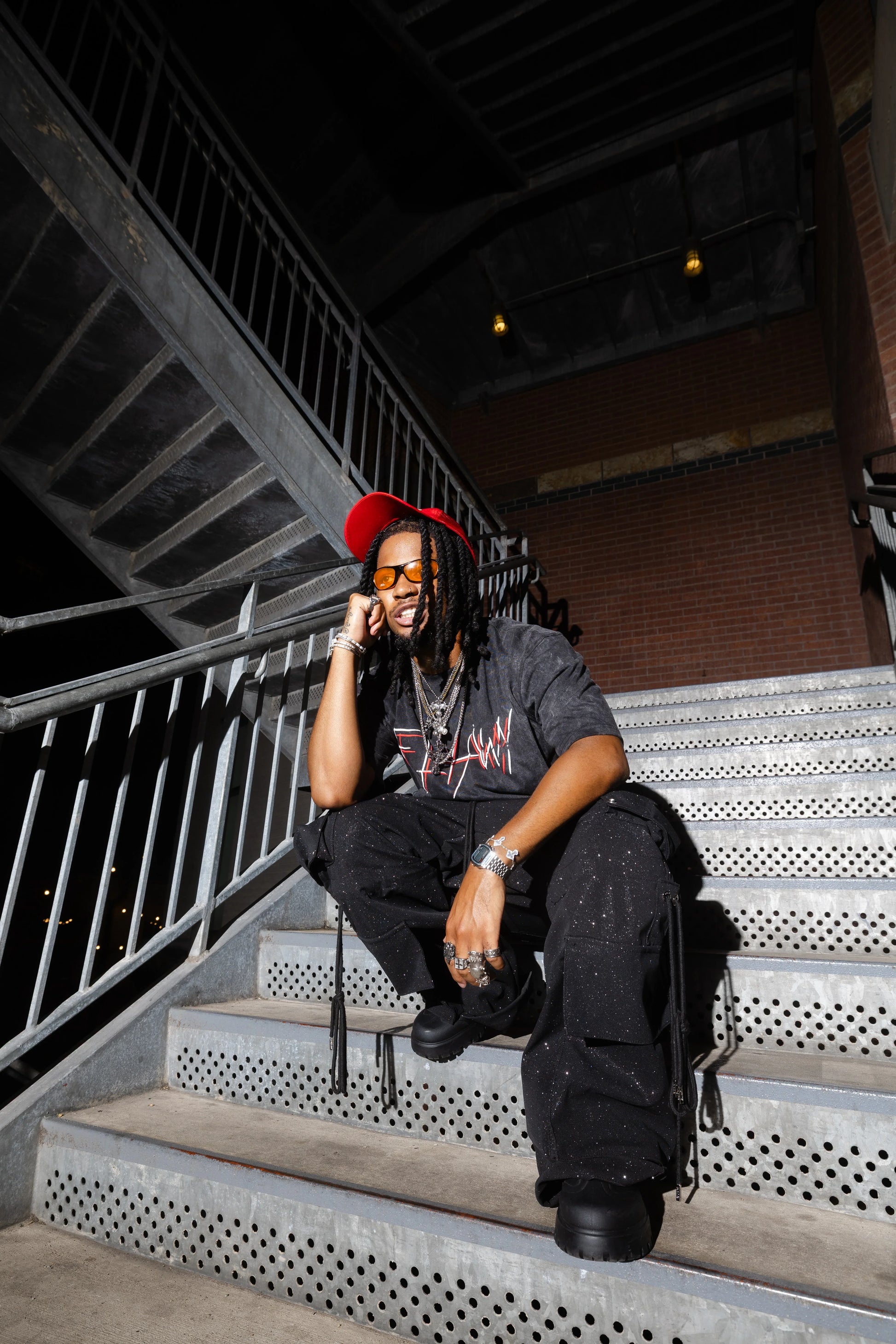 Oversized black acid-washed heavyweight tee with red and white graphic text, paired with black cargo pants and red cap.