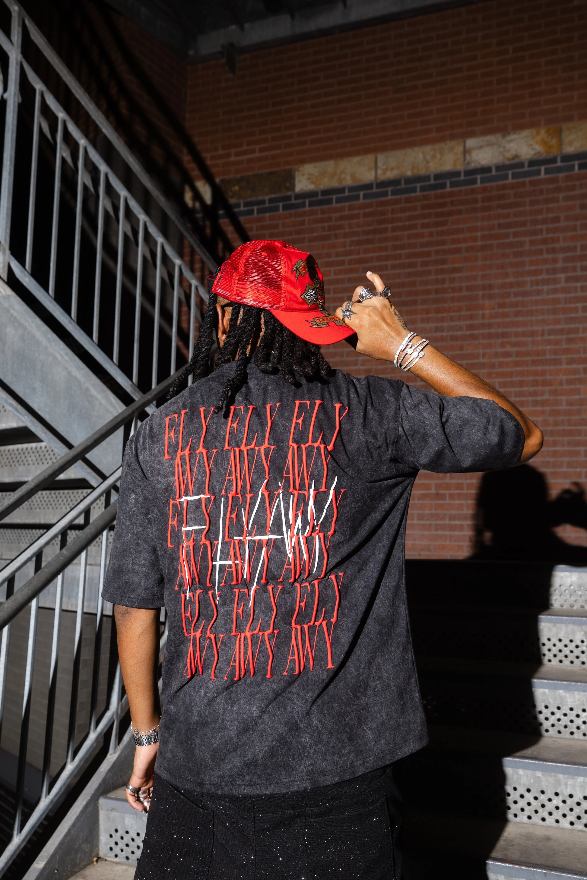 Oversized acid-washed black tee with bold red "FLY AWAY BOY" text graphic on back, heavyweight streetwear style.