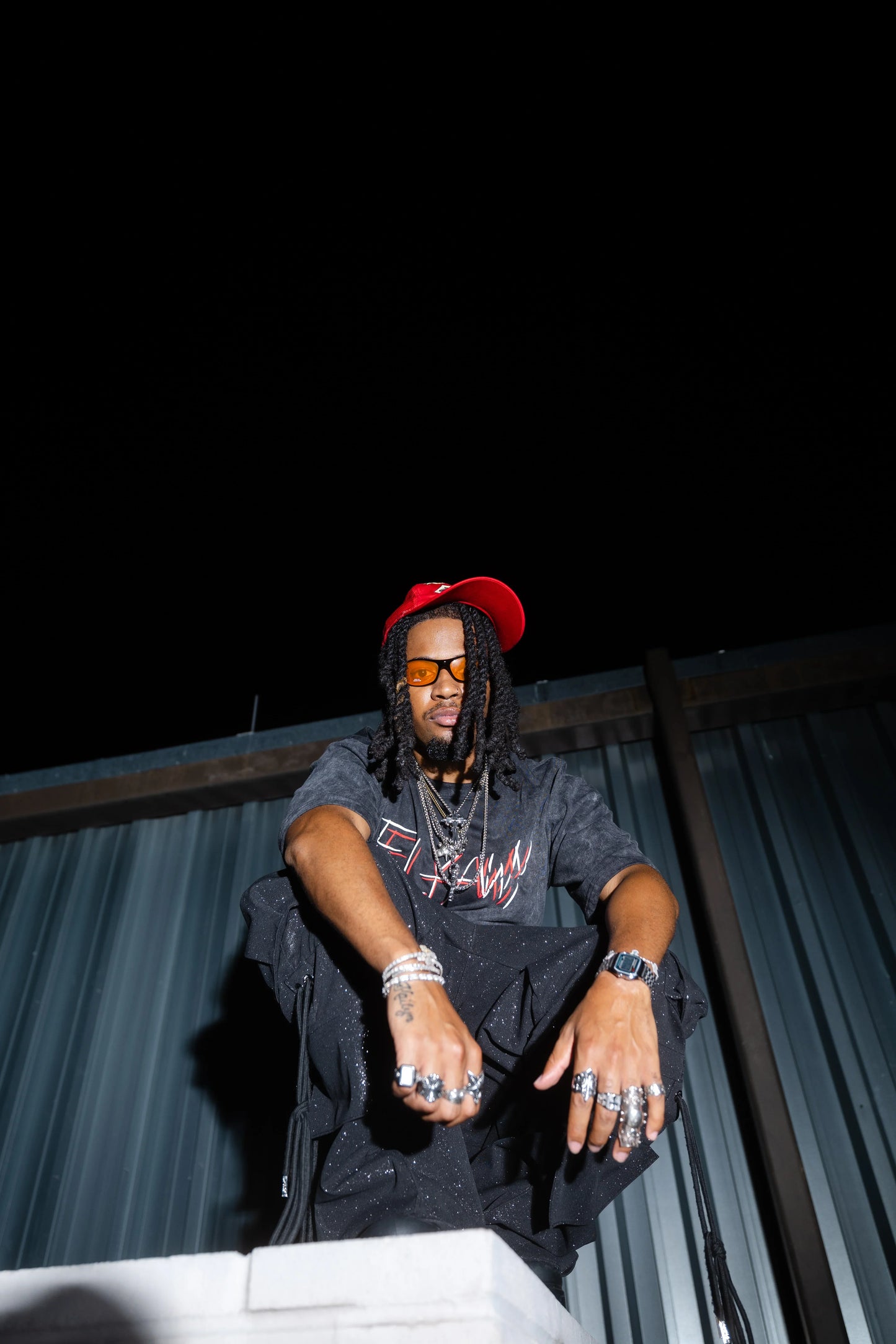 Oversized black acid-washed heavyweight t-shirt with red graphic text, worn with silver rings and a red cap.