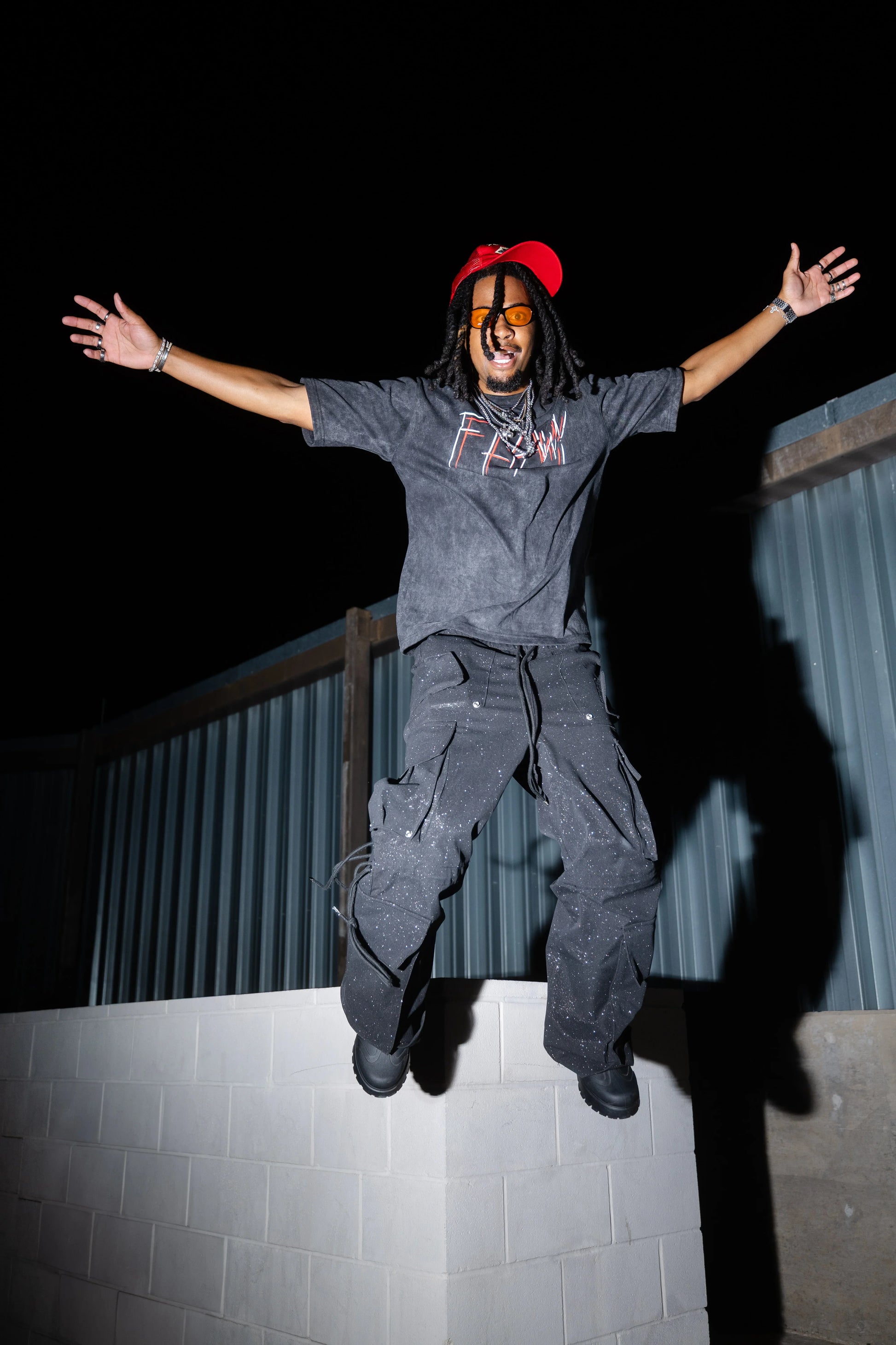Oversized acid-washed black graphic tee with red and white text, paired with loose black pants and a red cap.